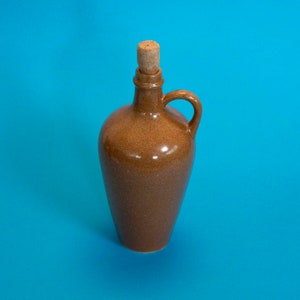 May include: A brown ceramic bottle with a cork stopper and a handle. The bottle is on a blue background.