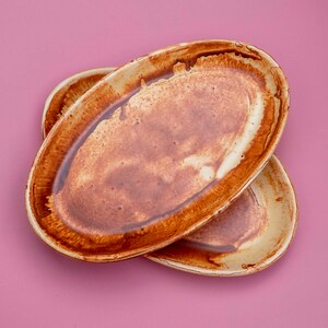 Pode incluir: Dois pratos de servir ovais de cerâmica com um esmalte castanho e bege. Os pratos estão empilhados um em cima do outro.