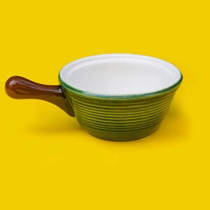 Peut inclure: Un petit bol en céramique vert et brun avec une poignée. Le bol a un intérieur blanc et est parfait pour servir des sauces ou des trempettes.