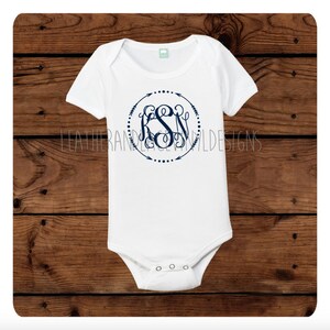 Könnte beinhalten: Weißer Baby-Strampler mit einem marineblauen Monogramm in einem Kreis mit Pfeilen und Punkten. Das Monogramm ist "KSN".