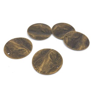 以下が含まれることがあります： 中央に小さな穴が開いた、テクスチャ加工された表面を持つ、丸い真鍮色の金属製のチャームが5つあります。