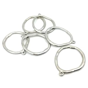 May include: A collection of five silver-toned metal rings with an irregular, organic shape. Each ring features a small, circular loop attached to the outer edge, designed for connecting components. The surface of the metal has a smooth, reflective finish.