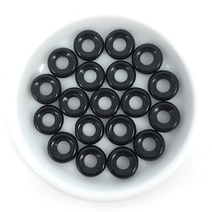 May include: A collection of black plastic ring-shaped beads, arranged in a circular pattern on a white plate.