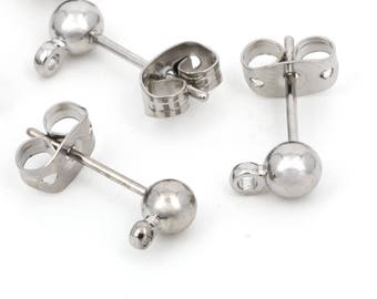 Puede incluir: Un conjunto de pendientes de botón plateados con forma de bola y cierre de mariposa. Los pendientes están dispersos sobre una superficie blanca, mostrando su diseño simple y minimalista. Los pendientes están hechos de un material metálico brillante.