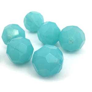 May include: A collection of light blue faceted beads. The beads have a round shape with multiple flat surfaces, creating a sparkling effect. The beads are scattered on a white surface.