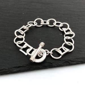 May include: A silver bracelet with a toggle clasp. The bracelet is made of a chain with alternating round and square links.