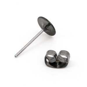 May include: A single black stud earring with a round disc and a straight post, next to a matching earring back. The earring and back are made of a dark metal and sit against a white background.