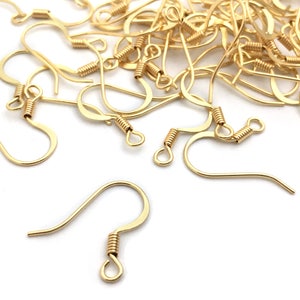 May include: A pile of gold-toned earring hooks with a spring closure. The hooks are scattered on a white surface.