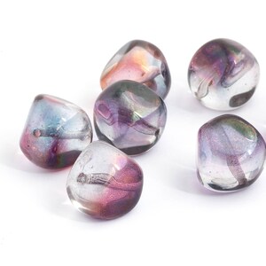 Puede incluir: Siete cuentas de vidrio iridiscente en tonos de morado, rosa y azul. Las cuentas son redondas y tienen una forma ligeramente irregular. Son perfectas para la elaboración de joyas u otros proyectos de artesanía.