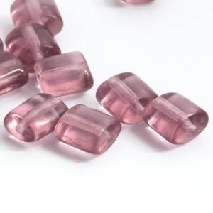 May include: A group of small, square, translucent purple glass beads. The beads have a frosted finish and are perfect for jewelry making or crafting.