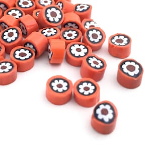 May include: A pile of orange and white ceramic beads with a flower design. The beads are scattered on a white background.