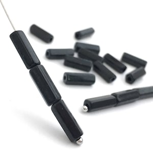May include: A close-up of black rectangular beads with silver caps. The beads are strung on a silver wire.