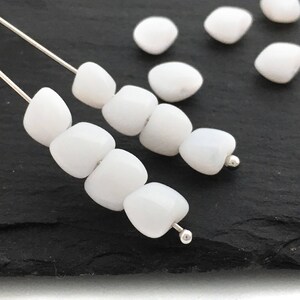 Könnte beinhalten: Eine Kette aus weißen Edelsteinperlen, die auf einem Silberdraht aufgefädelt sind. Die Perlen haben alle unterschiedliche Formen und Größen und sind in zufälliger Reihenfolge angeordnet.