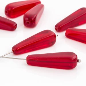 May include: A group of six red glass teardrop beads with a silver wire threaded through one of the beads.