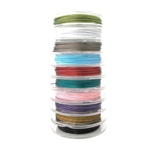 May include: A stack of spools of colorful cord in various colors, including green, white, gray, blue, red, teal, pink, purple, gold, and black. The spools are clear plastic and the cord appears to be a thin, flexible material.