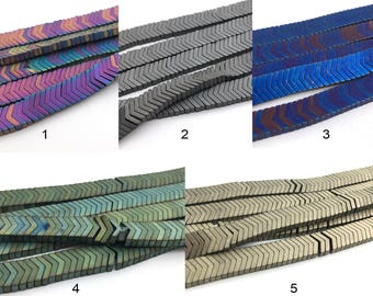 Peut inclure: Gros plan sur cinq brins de perles en forme de chevrons de différentes couleurs. Les perles sont disposées en rangées, présentant des teintes irisées, grises, bleues, vertes et dorées. Ces perles sont adaptées à la création de bijoux.