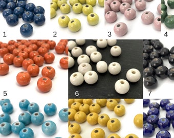 Puede incluir: Un conjunto de cuentas de cerámica en varios colores: azul marino, amarillo, rosa, verde, naranja, blanco, negro, turquesa y amarillo oscuro. Cada cuenta es redonda con un agujero en el centro, ideal para bisutería o manualidades.