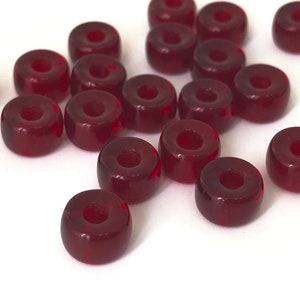 May include: A group of 17 red glass beads, each with a hole in the centre. The beads are scattered on a white surface.