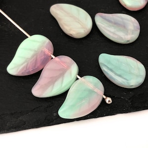 May include: A collection of iridescent green and pink glass beads in a teardrop shape. The beads have a pearlescent finish and are strung on a silver wire.