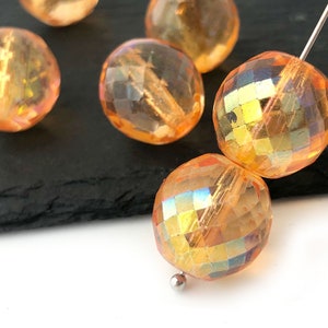 Könnte beinhalten: Eine Gruppe von irisierenden orangefarbenen Glasperlen mit facettiertem Design. Die Perlen sind rund und haben eine glänzende Oberfläche.