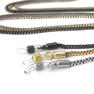 May include: Three eyeglass chains with different colored metal links. The chains are made of black, gold, and silver metal. Each chain has a clear plastic loop at each end.