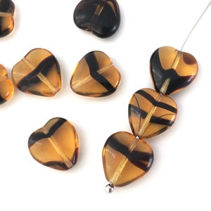 Può includere: Una collana di perline di vetro ambrato a forma di cuore con motivi a spirale neri e dorati. Le perline sono infilate su un filo d'argento.