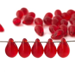 Könnte beinhalten: Eine Reihe von sechs roten Glasperlen in Tropfenform, die auf einem silbernen Draht aufgefädelt sind. Die Perlen sind durchscheinend und haben einen leichten Schimmer.