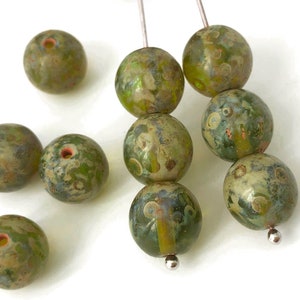 以下が含まれることがあります： 大理石模様の緑色のガラスビーズのネックレス。ビーズは丸く、中央に穴が開いています。ビーズは銀色のワイヤーに通されています。