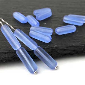 Puede incluir: Un grupo de cuentas de vidrio azul claro de forma rectangular. Las cuentas están dispuestas sobre una superficie negra.