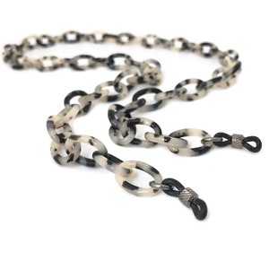 Puede incluir: Una cadena de plástico con estampado de carey en blanco y negro con extremos de goma negra para sujetar gafas.