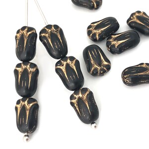 May include: Black tulip-shaped beads with gold-colored accents. The beads are strung on thin silver-colored wires, with a few loose beads scattered around. The beads have a glossy finish and a detailed floral design.