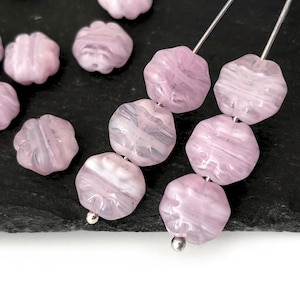 Puede incluir: Cuentas de vidrio rosa con un patrón de espiral, enhebradas en un alambre plateado. Las cuentas son facetadas y tienen una apariencia translúcida.