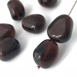 May include: A close-up of a strand of dark brown glass beads. The beads are smooth and have a slightly iridescent finish. They are strung on a silver wire.