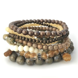 Pode incluir: Um conjunto de oito pulseiras feitas com contas marrons, bege e creme. As pulseiras são feitas com contas de diferentes tamanhos e formas.