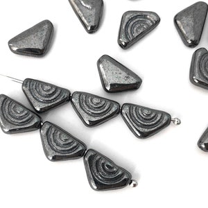 Puede incluir: Una hebra de cuentas de vidrio gris oscuro con un patrón circular texturizado. Las cuentas tienen forma de triángulos y están enhebradas en un alambre plateado.