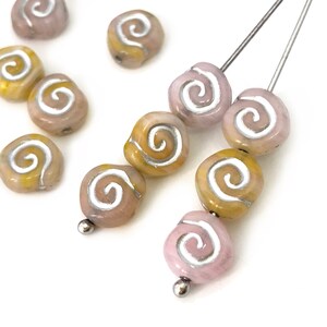 May include: Close-up of artisan beads in shades of pink and yellow with a silver spiral design. Some beads are strung on silver headpins. These unique beads are ideal for jewelry making and crafting projects.