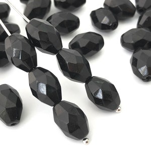 May include: A group of black faceted glass beads, some strung on a silver wire. The beads are oval shaped and have a glossy finish.