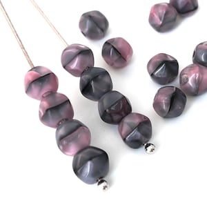 May include: Close-up of faceted beads in shades of gray and pink. The beads are strung on a thin, light-colored cord and scattered on a white surface. The beads have a geometric design with a mix of colors.