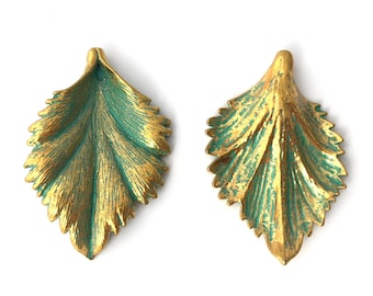 May include: A pair of gold leaf earrings with a green patina. The earrings are shaped like leaves with a detailed design.