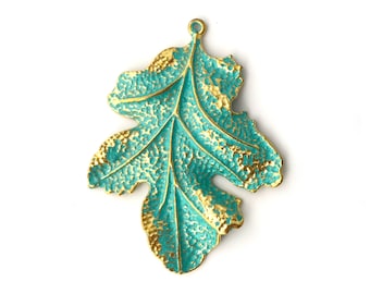 May include: A teal and gold leaf-shaped pendant. The pendant has a textured surface with a teal base and gold-colored edges and veins. It features a loop at the top for hanging. The leaf design is detailed and intricate.