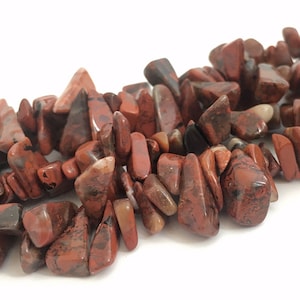 Peut inclure: Gros plan sur un fil de pierres précieuses de jaspe rouge. Les éclats sont un mélange de rouge profond et de brun, avec une forme irrégulière et polie. Les pierres sont enfilées, créant une esthétique naturelle et terreuse. Idéal pour la création de bijoux.