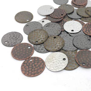 Puede incluir: Una colección de abalorios redondos de metal con textura martillada. Los abalorios son de varios tonos de plata, cobre y bronce. Cada abalorio tiene un pequeño agujero para sujetarlo a joyas u otras manualidades.
