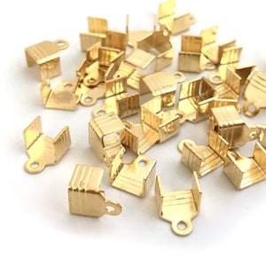 Puede incluir: Un montón de terminales de cordón de metal de color dorado. Los terminales son pequeños y tienen forma cuadrada con un pequeño bucle en un lado.