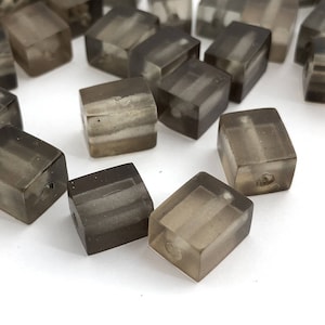 May include: A group of translucent gray cube-shaped beads with a striped pattern. The beads are scattered on a white surface.
