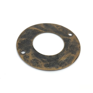 以下が含まれることがあります： 滑らかでわずかにテクスチャ加工された表面を持つ、真鍮色の丸い金属リング。リングの中央に穴があり、外縁に2つの小さな穴があります。