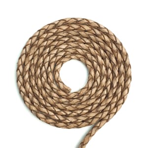 May include: Coiled, light brown braided leather cord against a white background. The cord is tightly woven, creating a circular pattern with a loose end extending outward. The texture of the leather is visible, showing variations in color and tone.