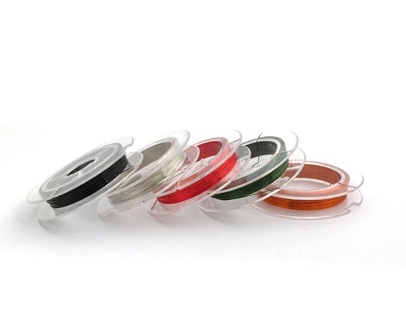 May include: Spools of colorful wire in various colors, including black, silver, red, green, and orange, are wound around clear plastic spools. The spools are arranged in a row on a white surface.