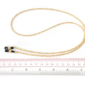 May include: Gold beaded eyeglass chain with black rubber end pieces. The chain is approximately 20 inches long.