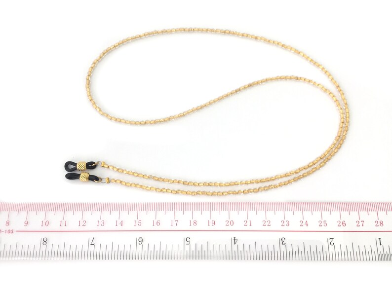 May include: Gold beaded eyeglass chain with black rubber end pieces. The chain is approximately 20 inches long.
