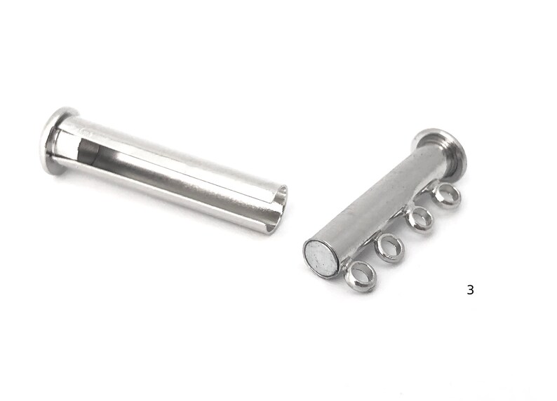 May include: Silver magnetic clasp for a multi-strand necklace. The clasp has four loops for attaching strands of beads or chain. The clasp is made of two pieces, one with a magnet and the other with a hollow tube.